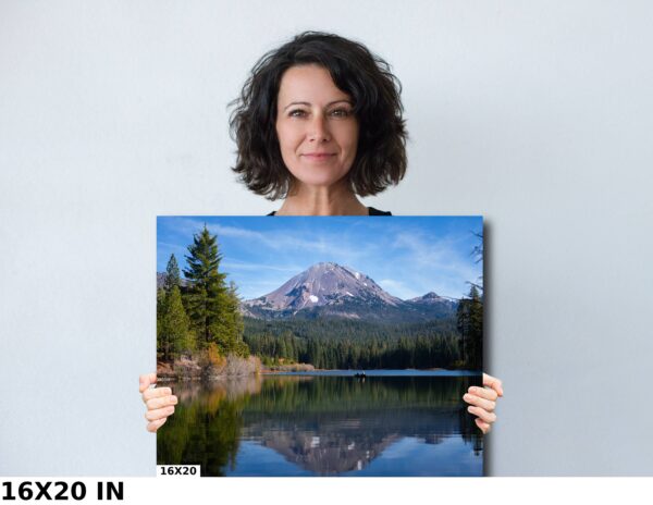 A woman holding up a picture of a mountain lake.