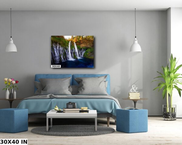 A bedroom with a blue bed and a painting of a waterfall.