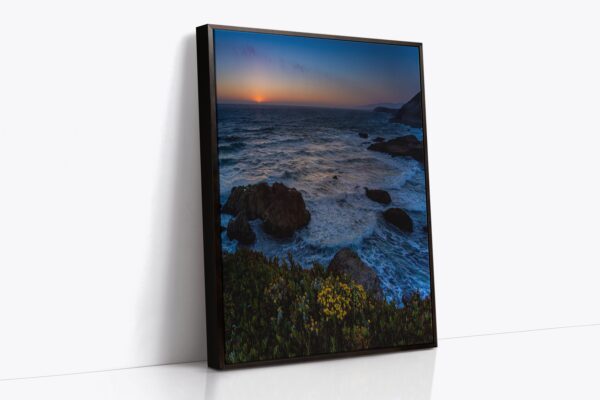 A picture of the ocean at sunset with rocks and flowers.