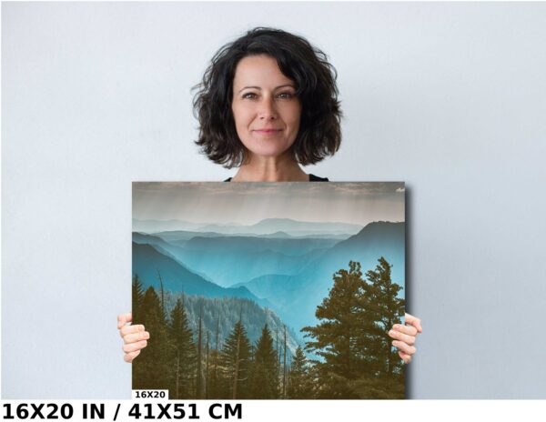 A woman holding up a painting of mountains and trees.