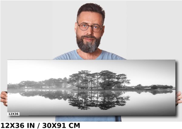 A man standing in front of a mirror with trees reflected on the water.