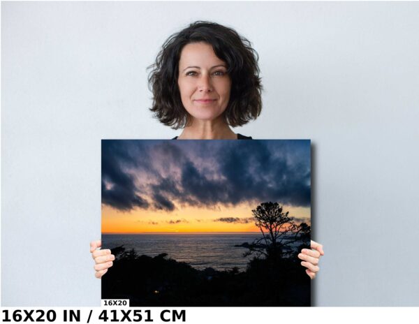 A woman holding up a picture of the ocean at sunset.