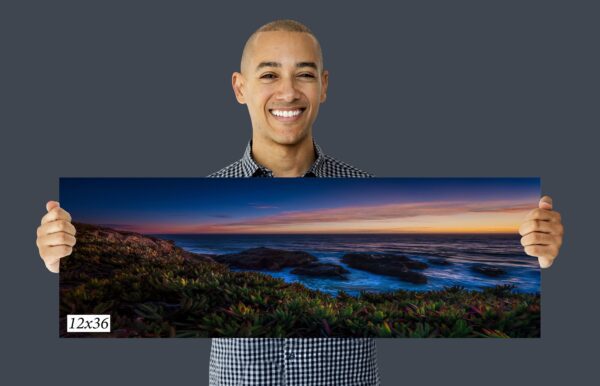 A man holding up a large canvas with a sunset picture on it.