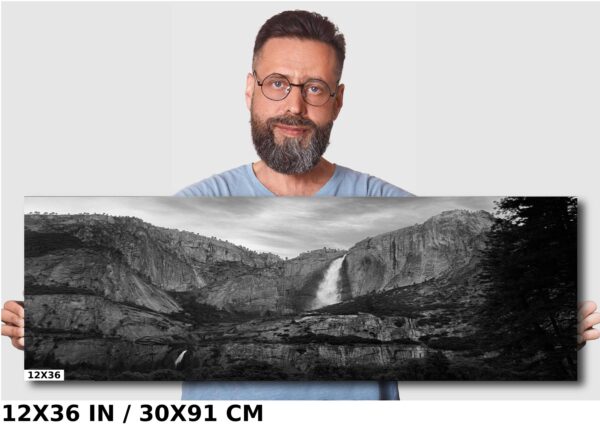 A man standing in front of a picture with mountains and water.