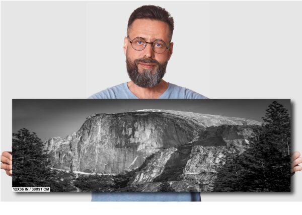 A man with glasses and beard standing next to a large rock.