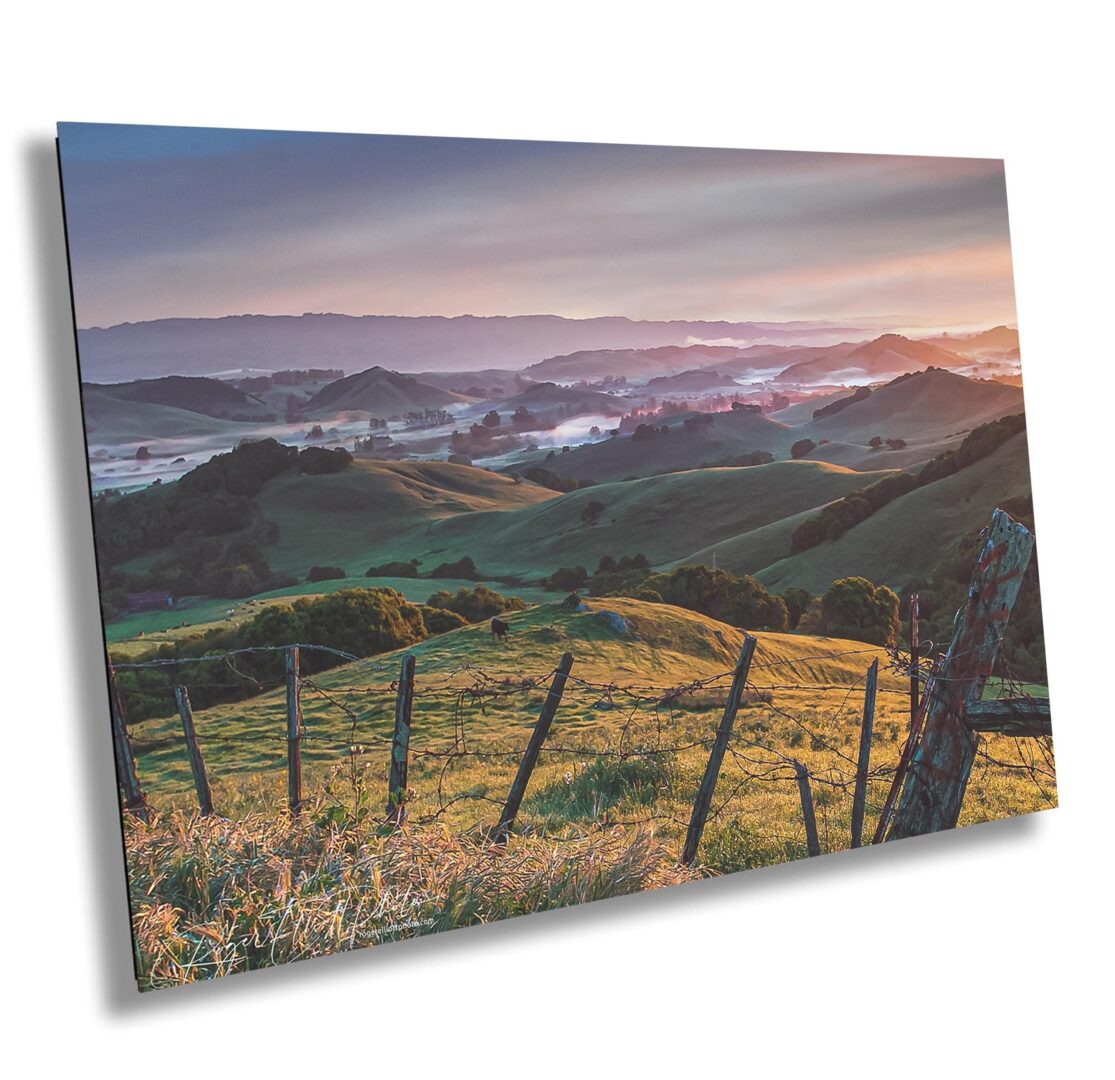 Golden sunrise over rolling hills near Petaluma, California. Layers of ridgelines, soft fog, and a rustic fence capture the peaceful start of day in Sonoma County.