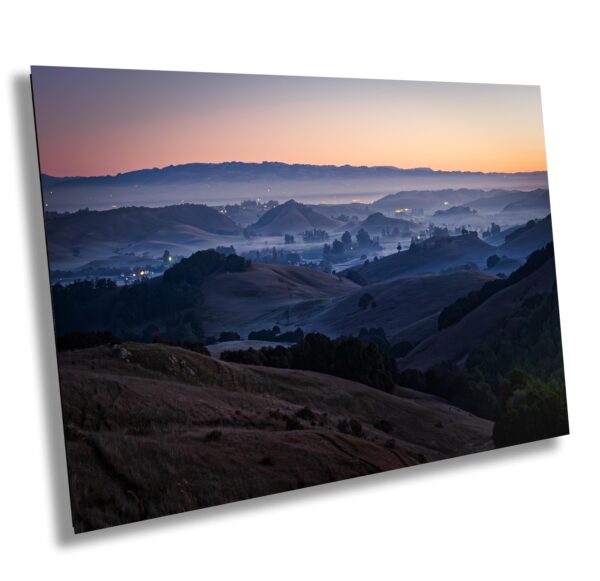 Pre-dawn view of Sonoma County with soft fog drifting through hills and valleys. Blue light, layered ridgelines, and town lights create a peaceful morning scene.