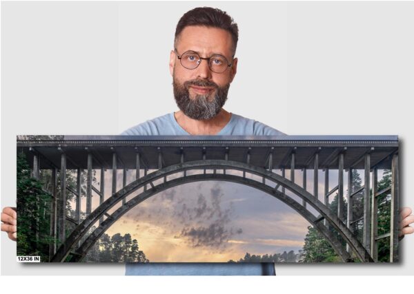 A man with glasses and beard standing next to a bridge.
