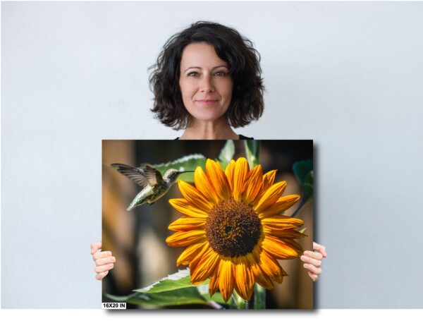 A woman holding a picture of a sunflower and hummingbird.